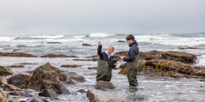 A man and a woman wearing gaiters standing in shallow ocean water
