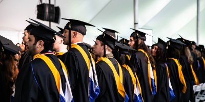 A side view of Salve graduate students standing in front of their chairs at commencement