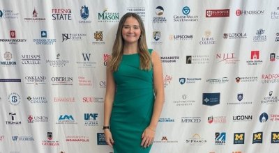 A woman in a green dress standing in front of a step and repeat