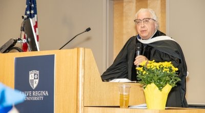Sacco in regalia speaking at a Salve Regina University podium.