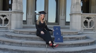 Megan wearing her grad cap on the back steps of Ochre Court, sitting with her three degrees from Salve.