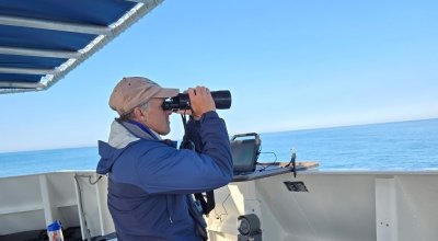 Chace on a boat looking out into the water with binoculars.