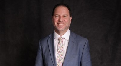 Professional headshot of Lorenz smiling in grey suit and colorful plaid tie.