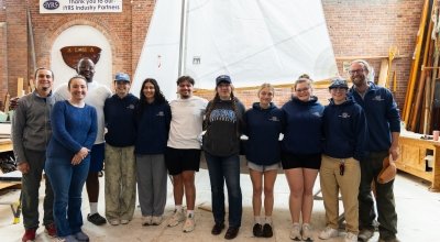 Group photo of the students and instructors in front of the boat they built from the ground up.