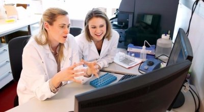 Jillian Wise and another collegue sitting in white lab coats discussing something they are viewing on the computer in front of them.