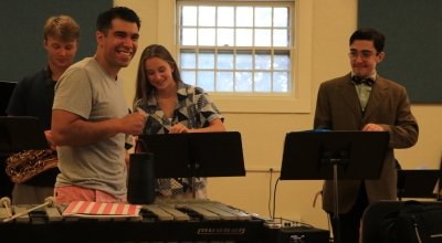 Students smiling in a music room behind their music stands.