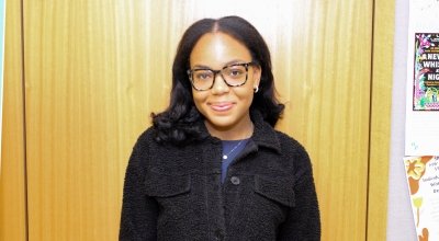 Headshot of Marsara in black jacket, standing in front of wooden wall.