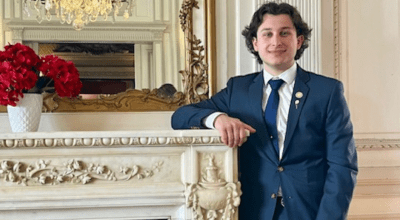 Photo of Silva in a suit smiling and leaning against a white fireplace mantle.