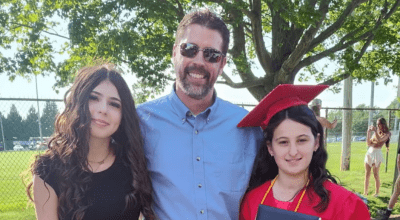 Corey smiling next to his daughters at a high school graduation.