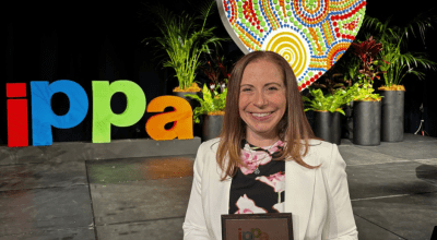 Perry smiling holding her iPPa award in front of a rainbow IPPa sign.