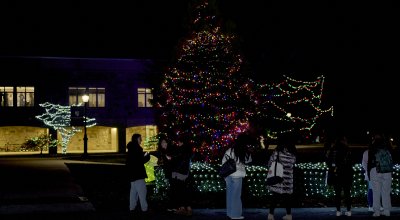 photo of tree light up for christmas outside with students gathered near.