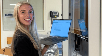 Cara working at the hospital smiling toward camera holding a computer.