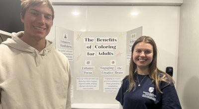 Anderson and man standing in front of a poster board smiling.