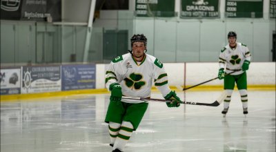 Connolly on the ice rink in his green and white hockey uniform, holding his stick.