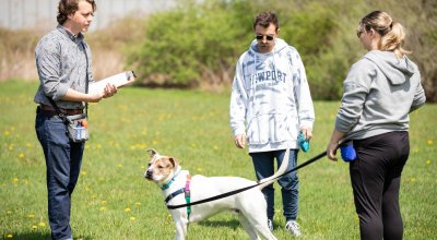 two students and professor outside in field, one with a white and tan dog on a leash.