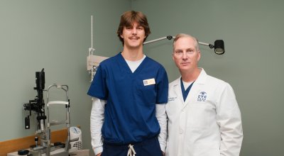 Optometrist and intern standing in eye exam room posing for photo.