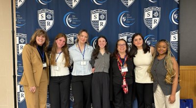 Jessicka and other students smiling in front of a We Mean Business Day backdrop.