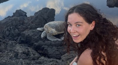 Bermingham smiling on rocks next to a sea turtle.
