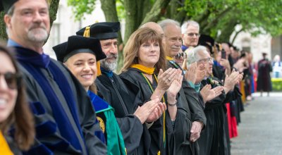 faculty in their regalia clapping as students walk down to graduation.