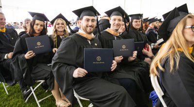Students at the Commencement ceremony sitting and smiling in their regalia with their diplomas in hand.