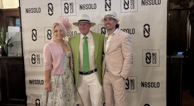 group photo of three people in pink and green outfits in front of a NOSOLO backdrop, for a Kentucky Derby fundraising event.