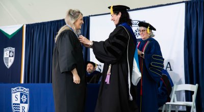 Student and faculty in black robes at nursing pinning ceremony