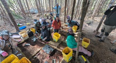 Students smiling in their test pits during an excavation in the woods.