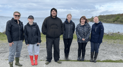 group photo of six people outside in front of the ocean.