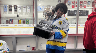 Aryana in hockey jersey holding large trophy.