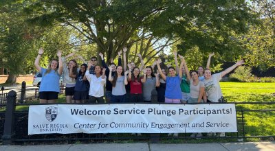 Service Plunge participants pose behind a Salve welcome banner with their hands raised.
