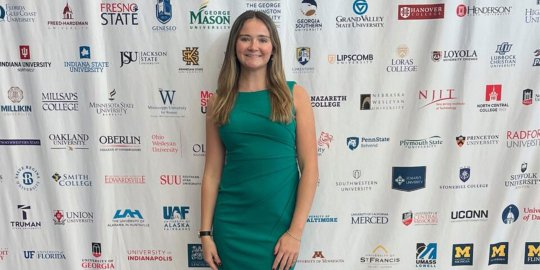 A woman in a green dress standing in front of a step and repeat