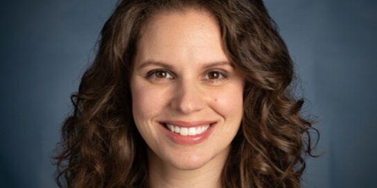 Professional headshot of Parks in yellow shirt and black cardigan.