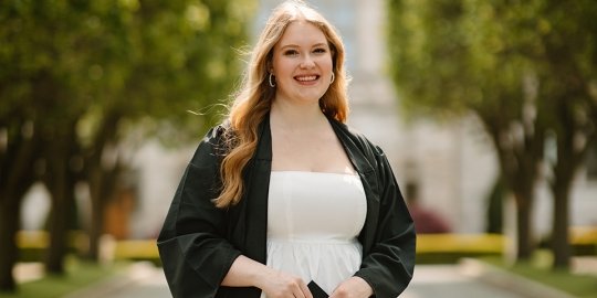 Professional photo of Pier smiling in graduation gown in front of Ochre Court