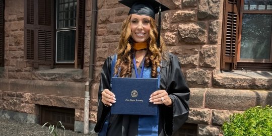 Sandra Mota in graduate regalia holding her diploma