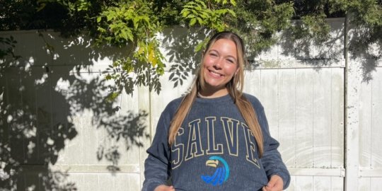 female student outside surrounding by green foliage in salve sweatshirt