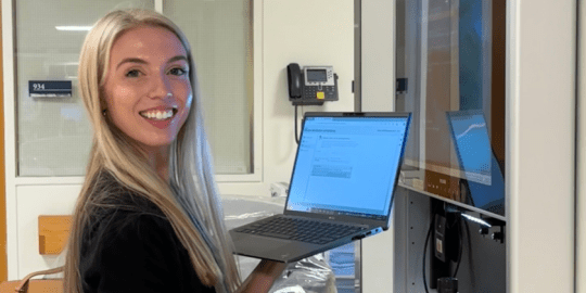 Cara working at the hospital smiling toward camera holding a computer.