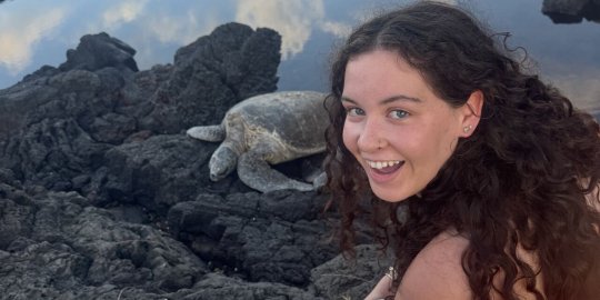 Bermingham smiling on rocks next to a sea turtle.
