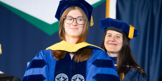 Behavior Analysis Ph.D. graduate Hannah Grey on stage at commencement in full doctoral regalia 