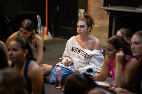Dance students sit on stage and take notes 