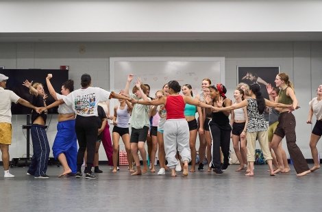 Group of students holding hands and dancing in front of a whiteboard
