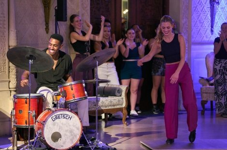 Smiling student dancing in front of a jazz drummer
