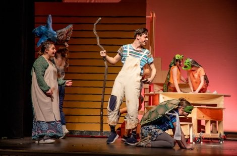 actors in animal costumes surround a boy in white overalls with a staff