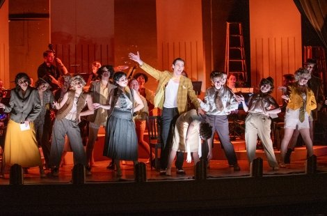 Group performing a musical number from 'Chicago' in gold and grey costumes
