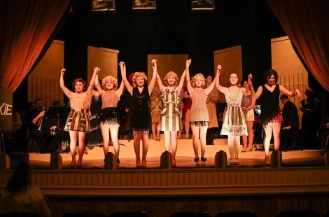 Seven actresses in a line holding hands in the air