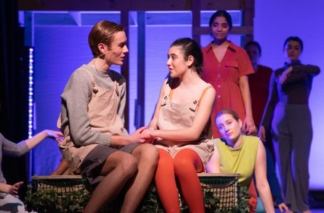 Two actors sitting on stage in burlap tops, one with orange tights