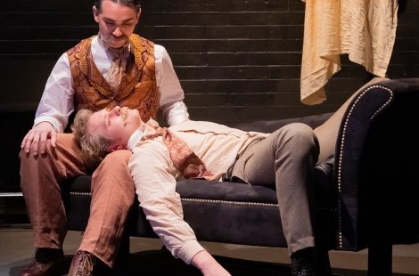 Two actors on a bench, one lying with his head in the other's lap