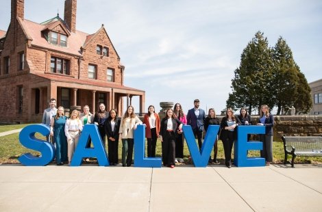 Students pose outdoors behind big blue letters spelling out 'Salve'