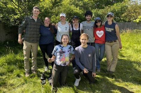 Nine students pose with archaeology gear in front of trees