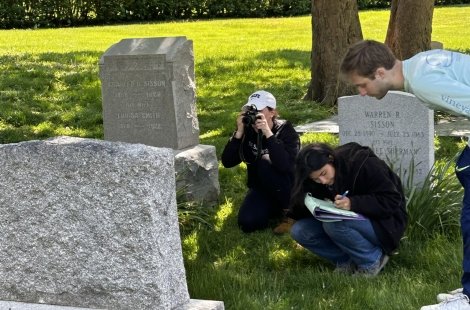 students crouched in front of gravestones taking photos