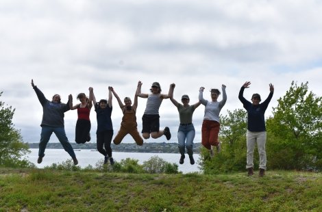 Eight students holding hands and jumping in front of water